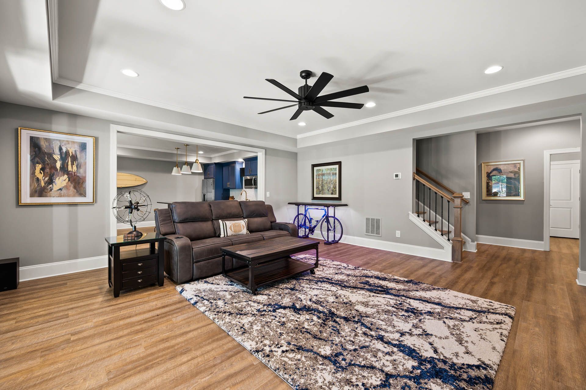 A modern living room with hardwood floors, a gray reclining sofa, and a large rug. A bicycle is set up behind the sofa.