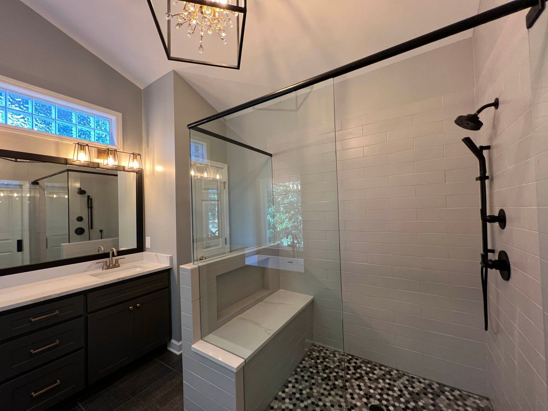Modern bathroom with a large glass shower. Dark vanity and hardware contrast with light-colored tile and a pebble shower floor.