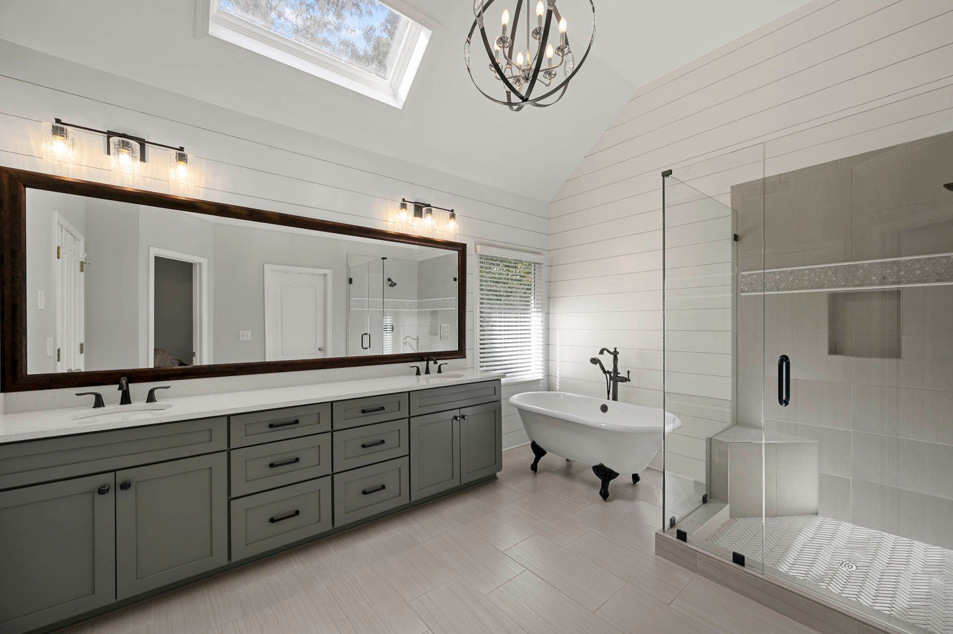 Spacious, modern bathroom with a vanity, soaking tub, and walk-in shower. White walls, light wood floor, gray cabinets.