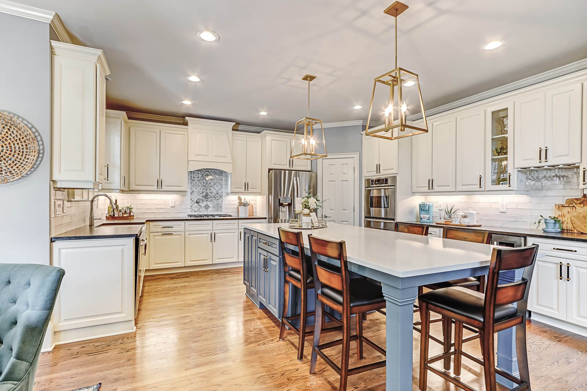 Spacious kitchen with white cabinets, a blue island with stools, and hardwood floors. Overhead lighting illuminates the space.