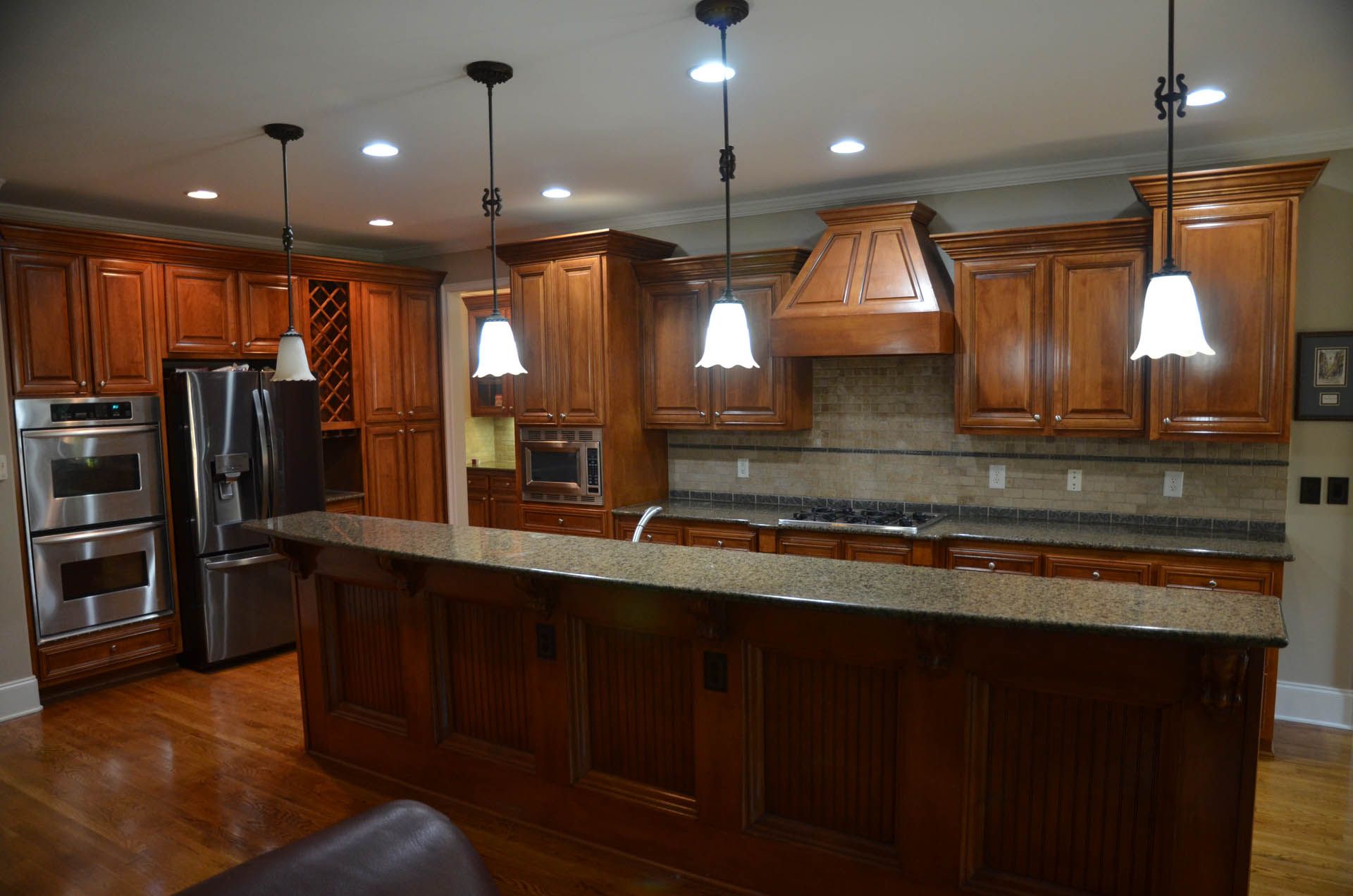 A well-lit kitchen with dark wood cabinets, granite countertops, and a large island. Stainless steel appliances are visible.