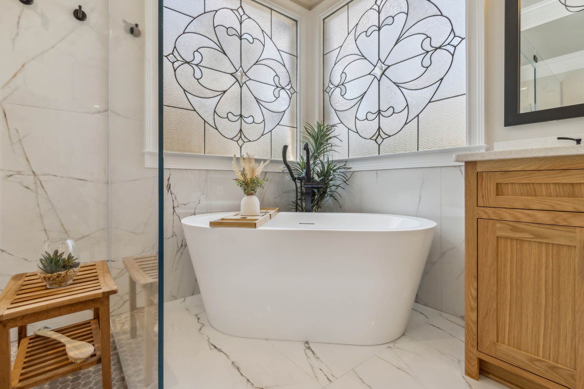 Bathroom with white freestanding tub, light wood cabinet, and decorative stained glass windows. Marble tiling.