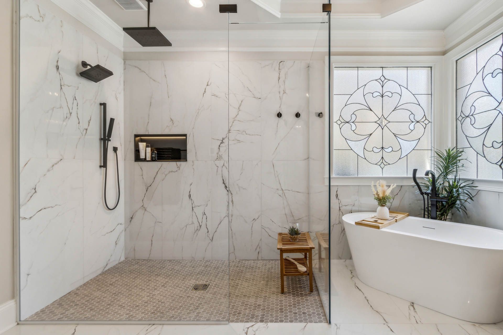 Luxurious modern bathroom with marble tile shower, glass door, and freestanding white bathtub.