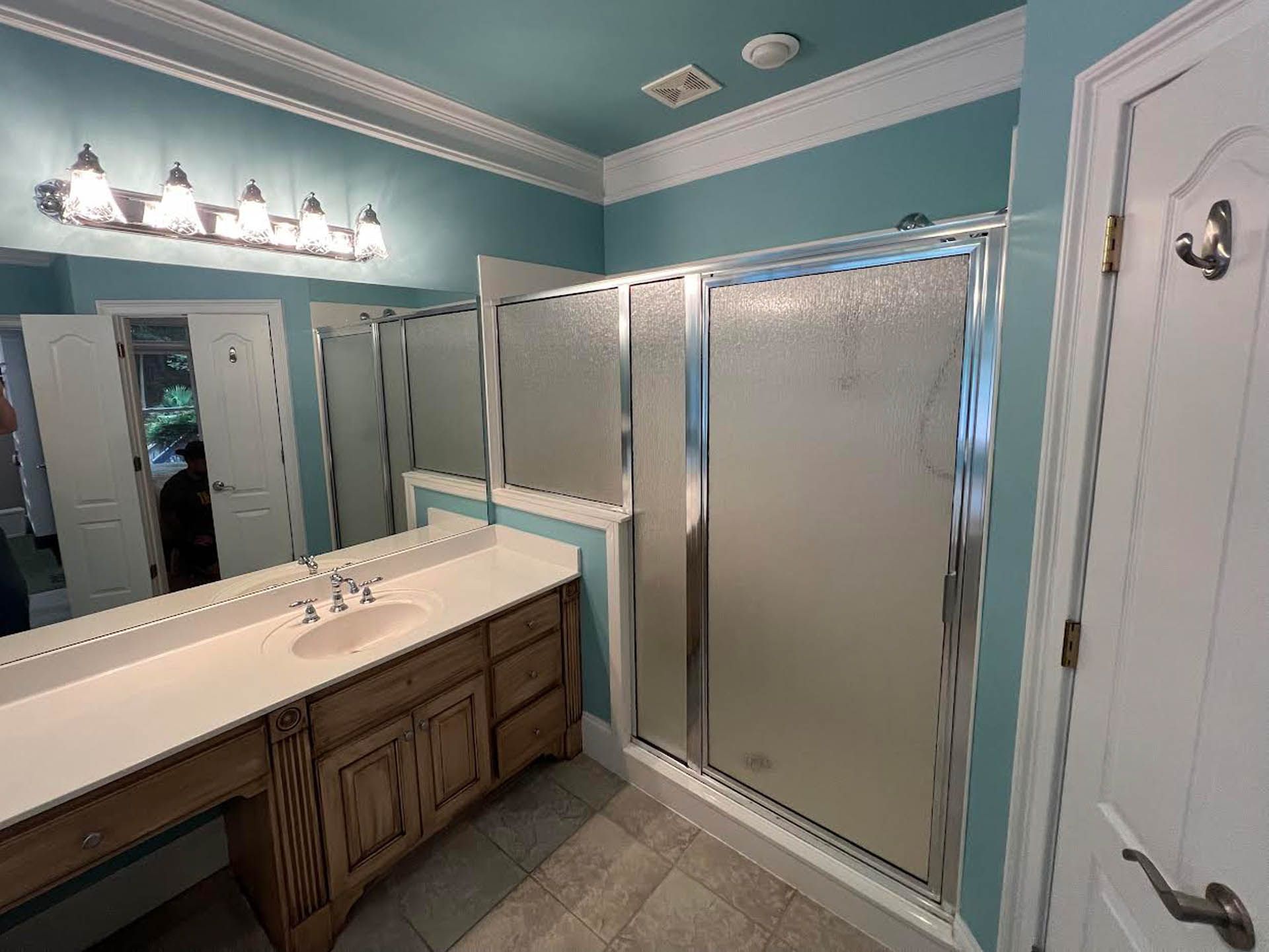Bathroom with light blue walls, white trim, vanity, shower, and large mirror.