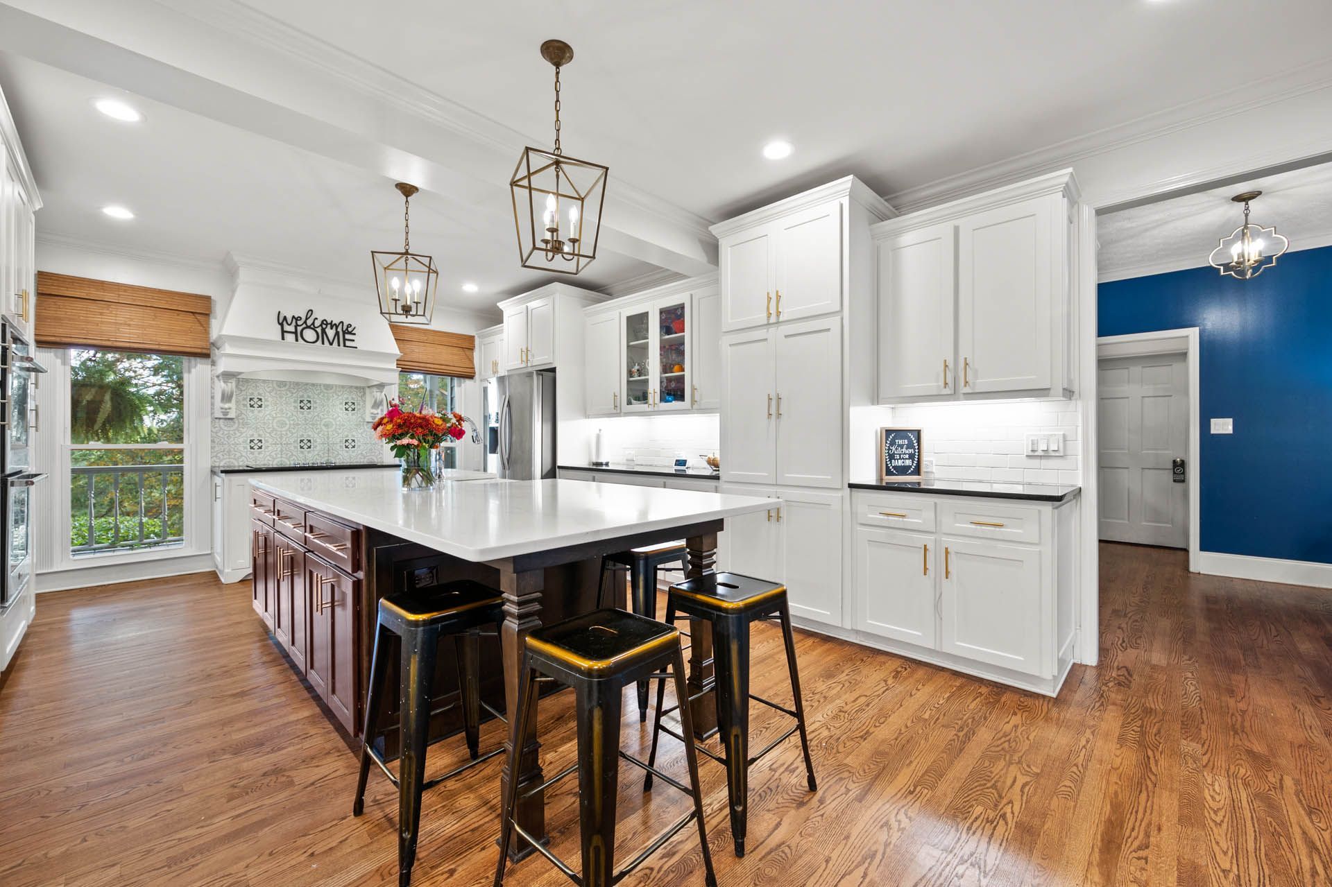 Spacious kitchen with white cabinetry, a large island, and hardwood floors. Features include a stainless steel refrigerator, and decorative light fixtures.