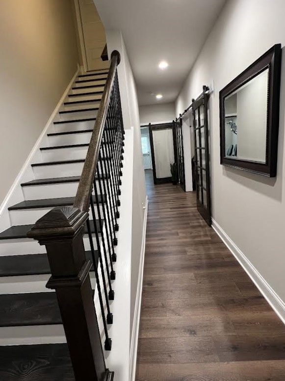 Narrow hallway with dark wood flooring, a staircase on the left, and two sliding glass doors ahead. A mirror hangs on the right wall.