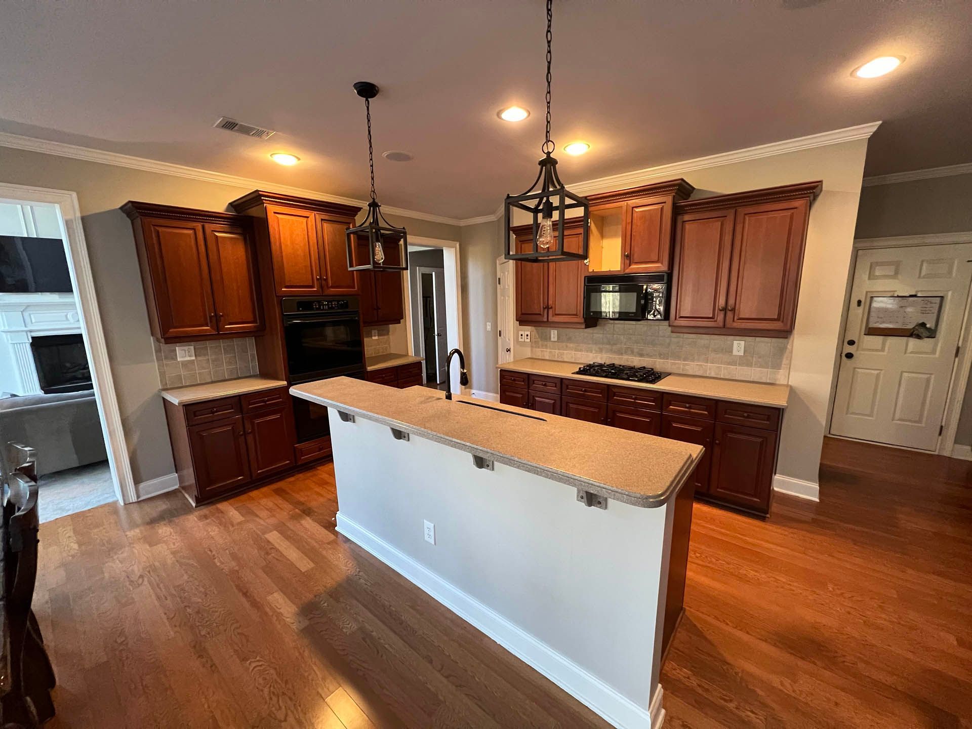 A kitchen with dark wood cabinets, light countertops, and a center island. Hardwood floors and two pendant lights are visible.