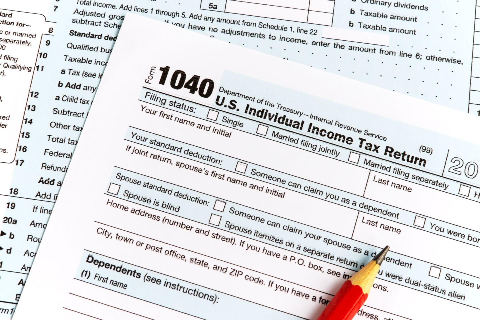 A close-up of a U.S. 1040 tax form with a pencil on top, paperwork in background.