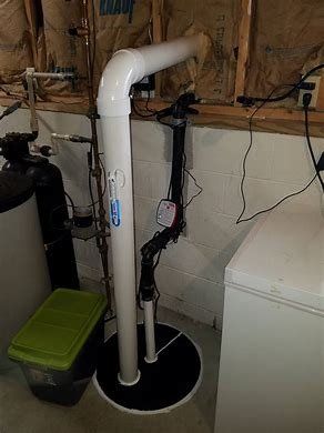 A white pipe is sitting in a basement next to a green box.