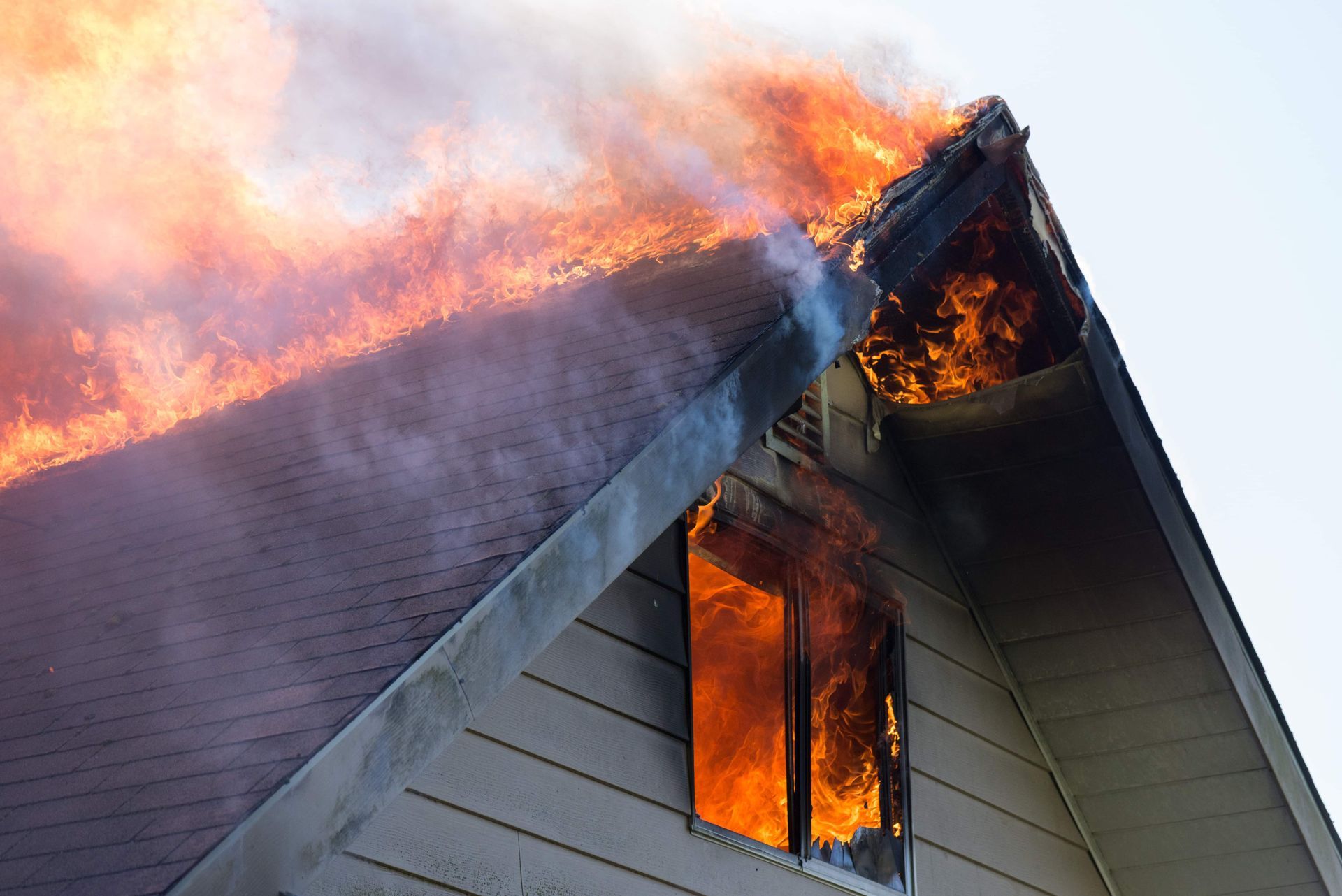 House roof engulfed in flames, smoke billowing into the sky.