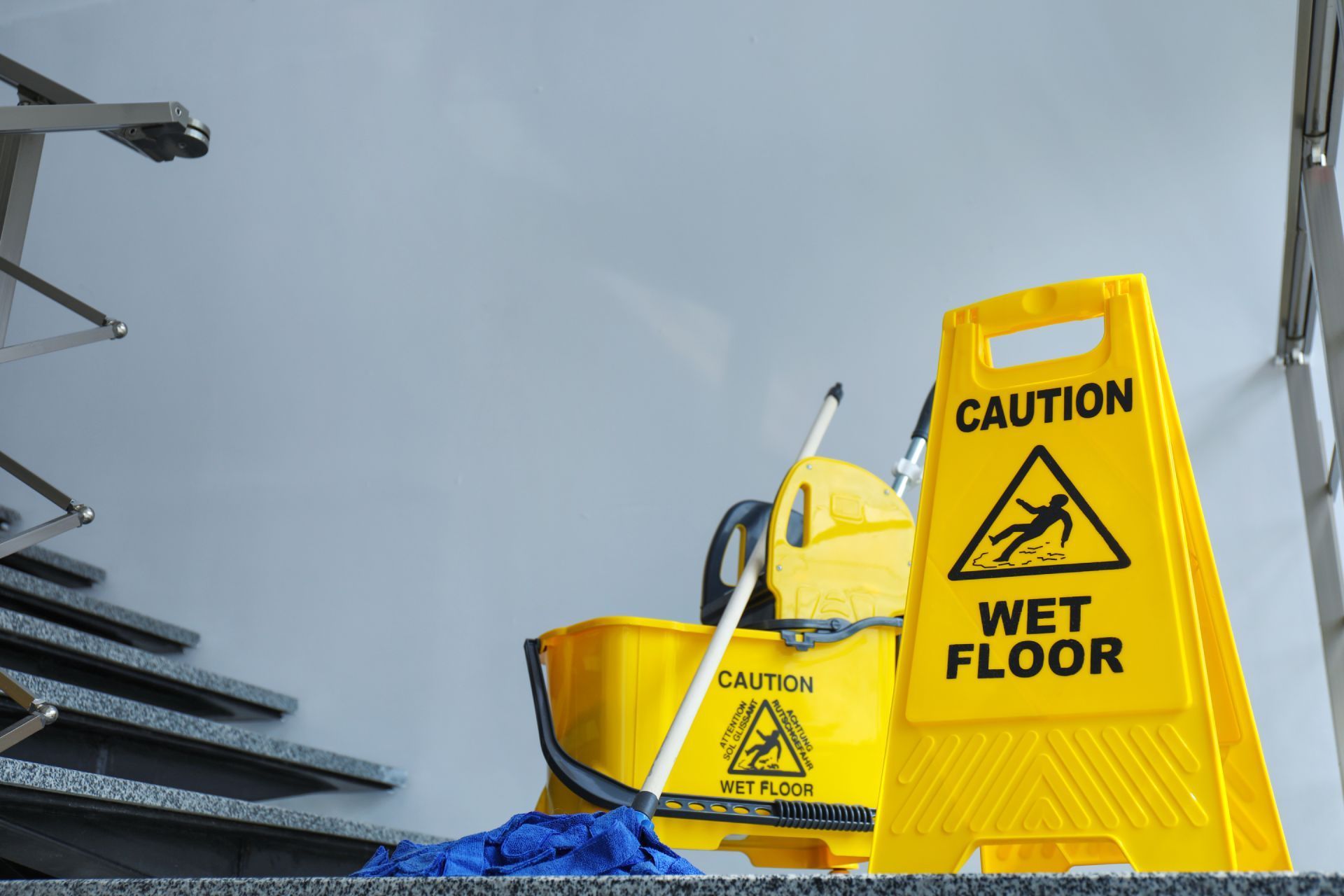 Janitor mopping a shiny floor beside a yellow cleaning cart in a hallway