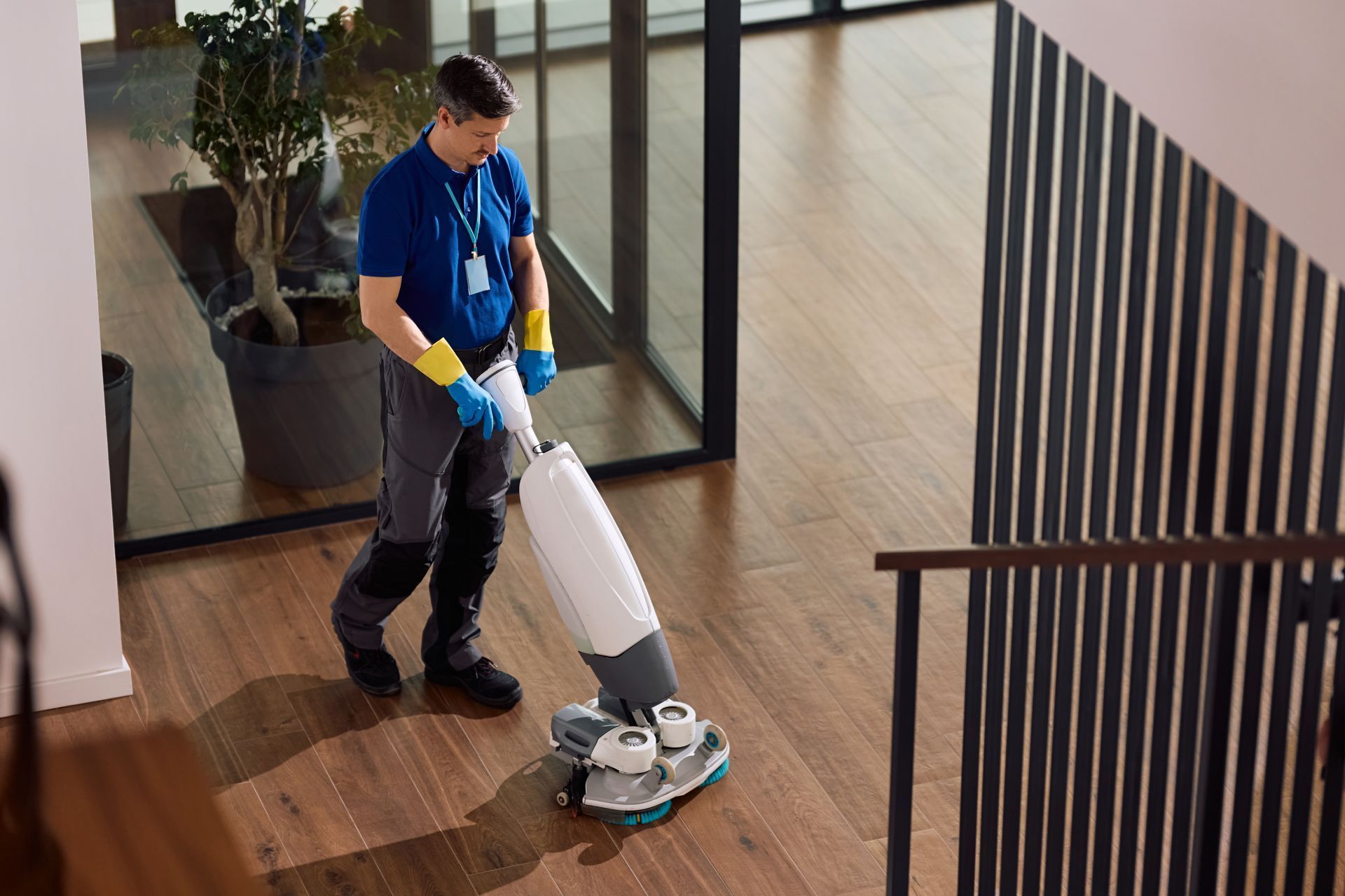 Janitor mopping a shiny floor beside a yellow cleaning cart in a hallway