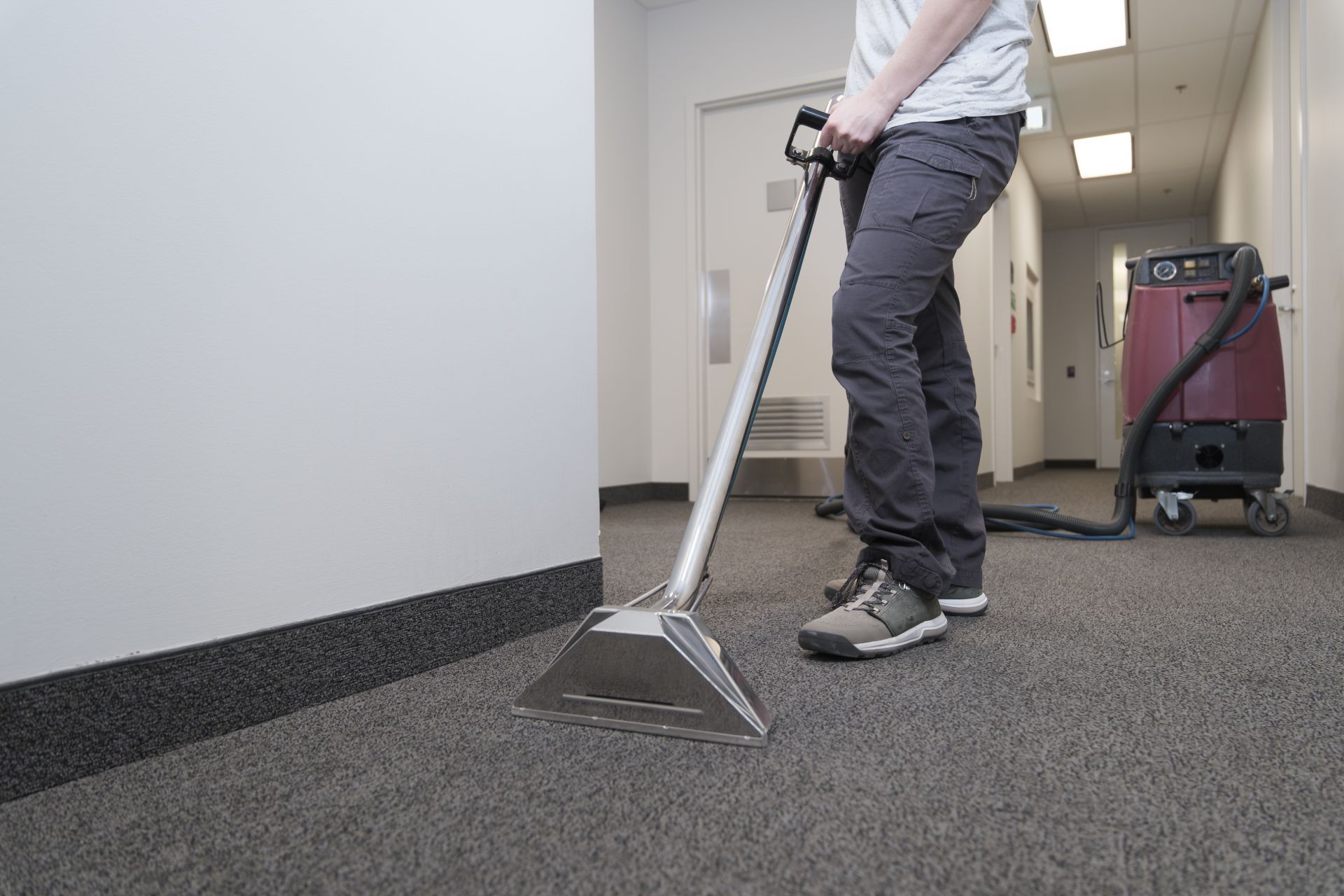Janitor mopping a shiny floor beside a yellow cleaning cart in a hallway
