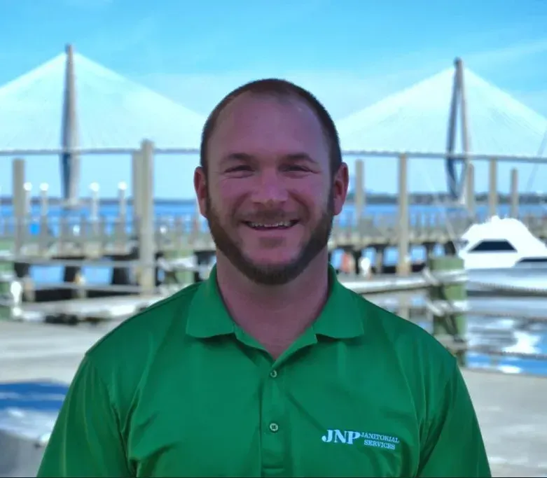 Smiling man in a green polo standing by a marina with a bridge in the background
