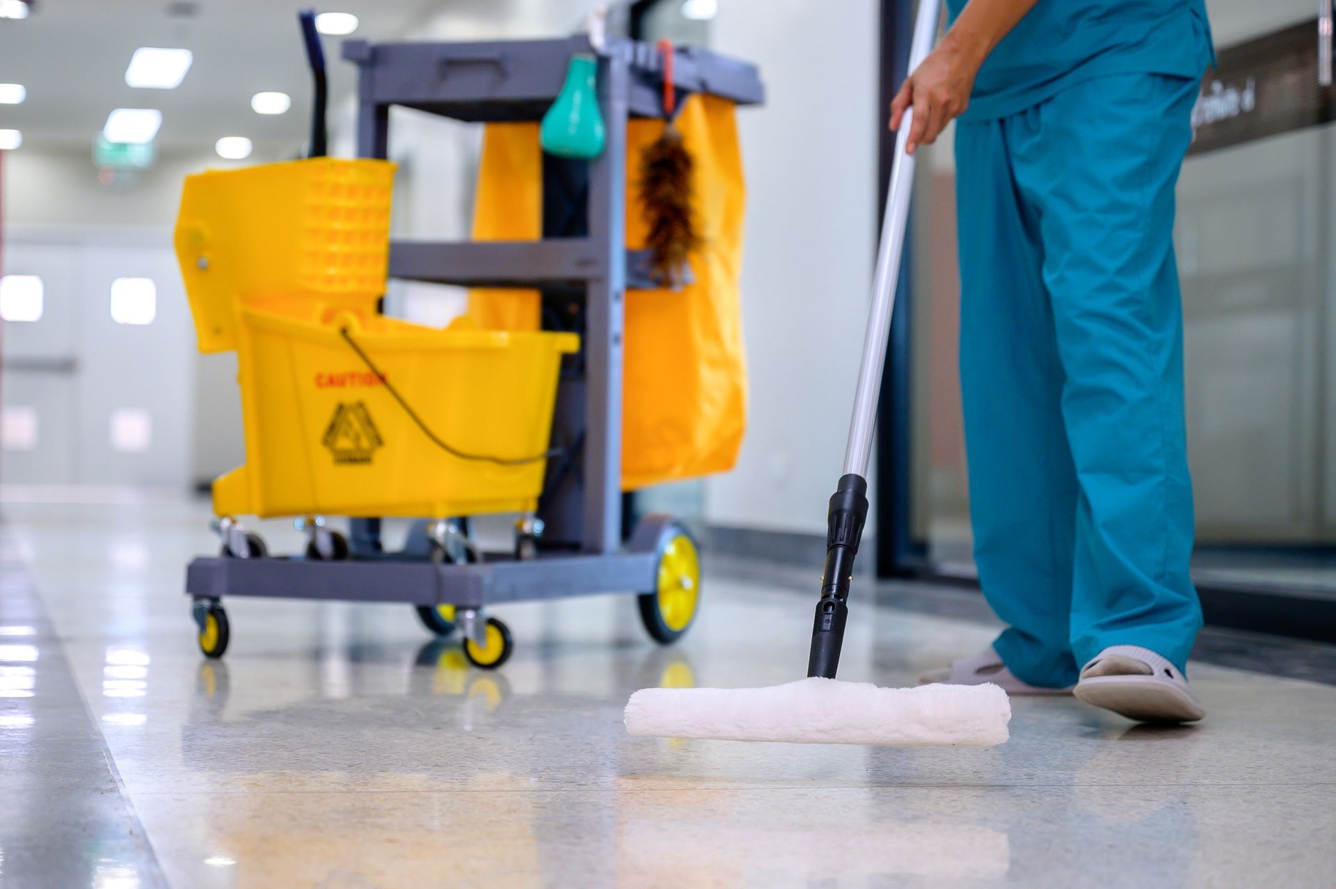 Janitor mopping a shiny floor beside a yellow cleaning cart in a hallway