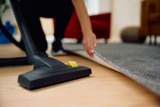 Person vacuuming carpet edge beside hardwood floor with a black vacuum cleaner