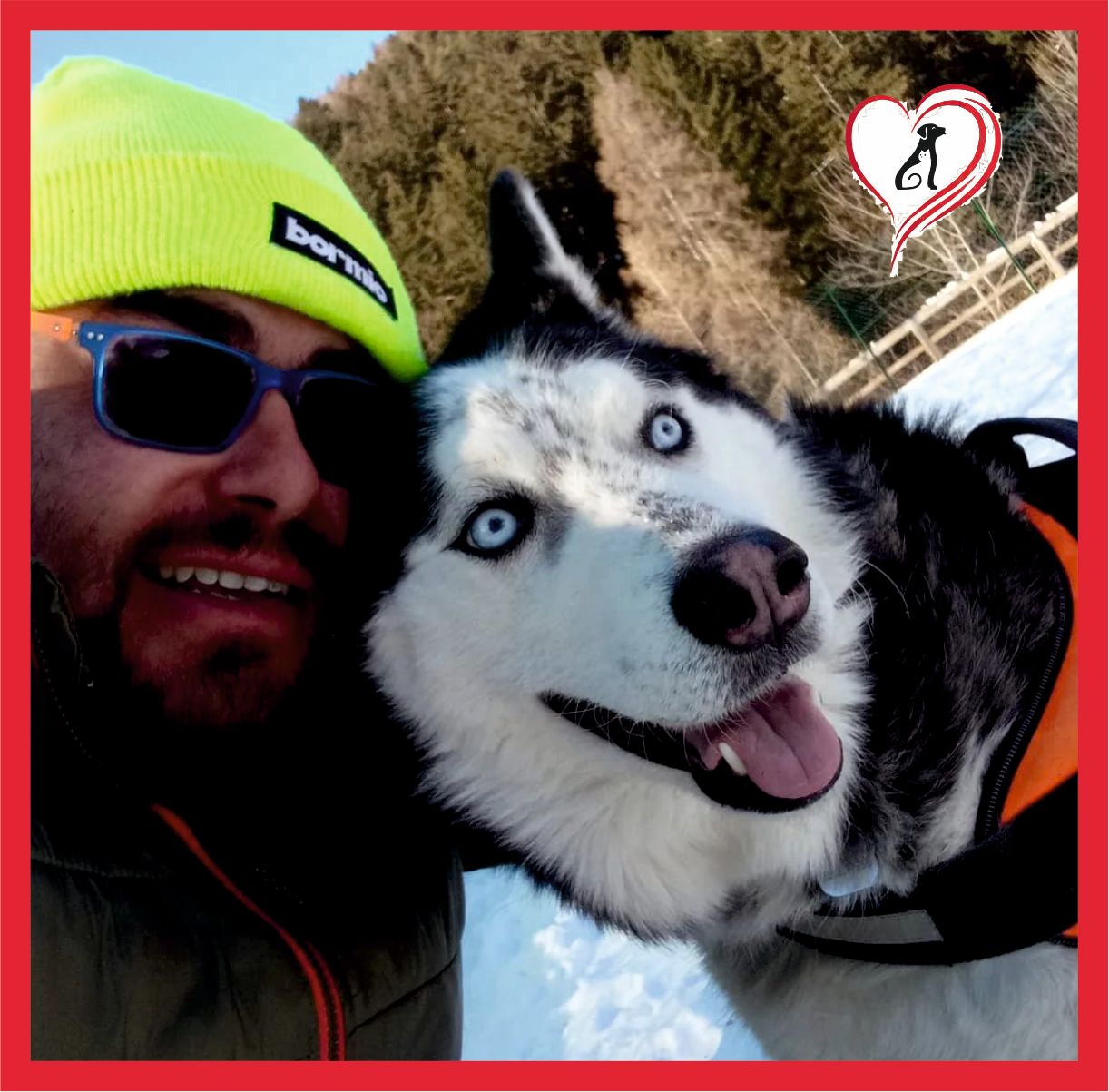 Un uomo che indossa occhiali da sole e un berretto giallo è in piedi accanto a un cane husky