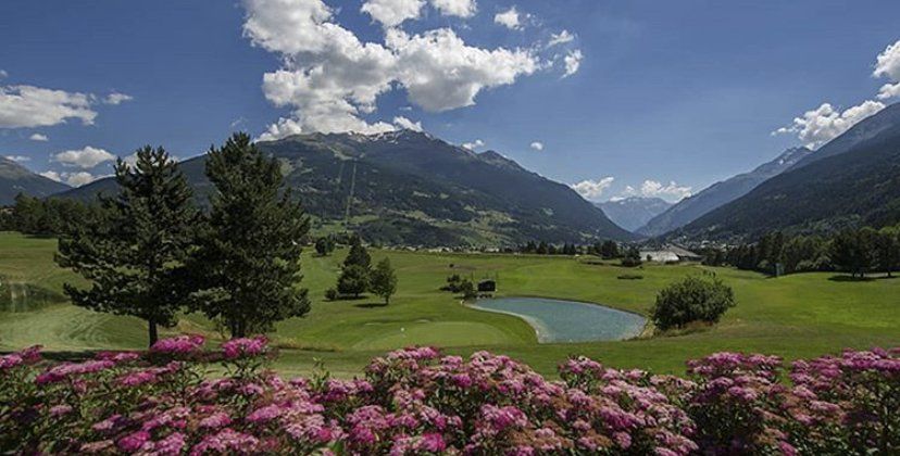 Un campo da golf con montagne sullo sfondo e fiori rosa in primo piano.