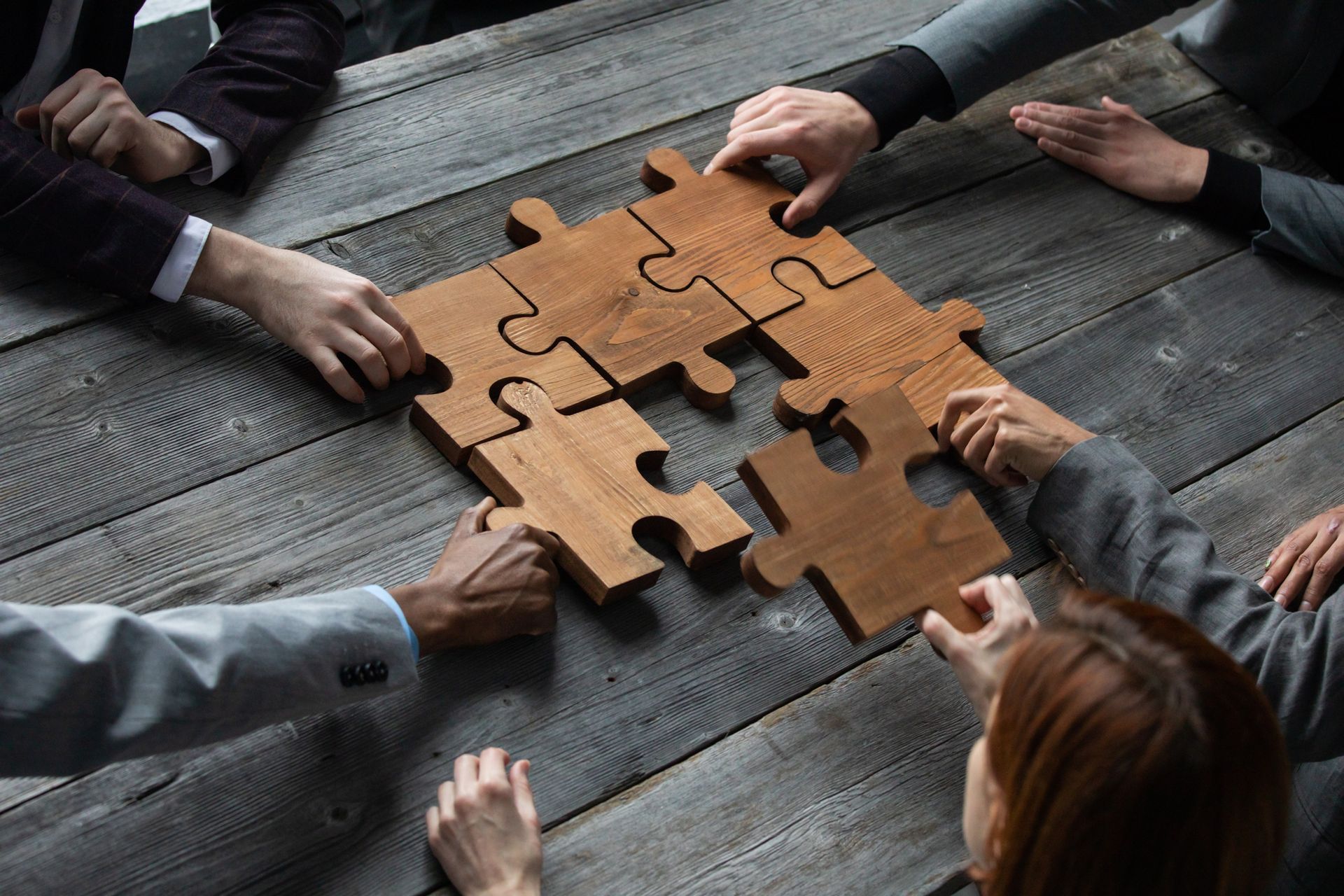 Hands fitting wooden puzzle pieces on a wooden table.
