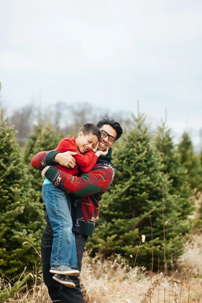 A father hugging his young son among evergreen trees