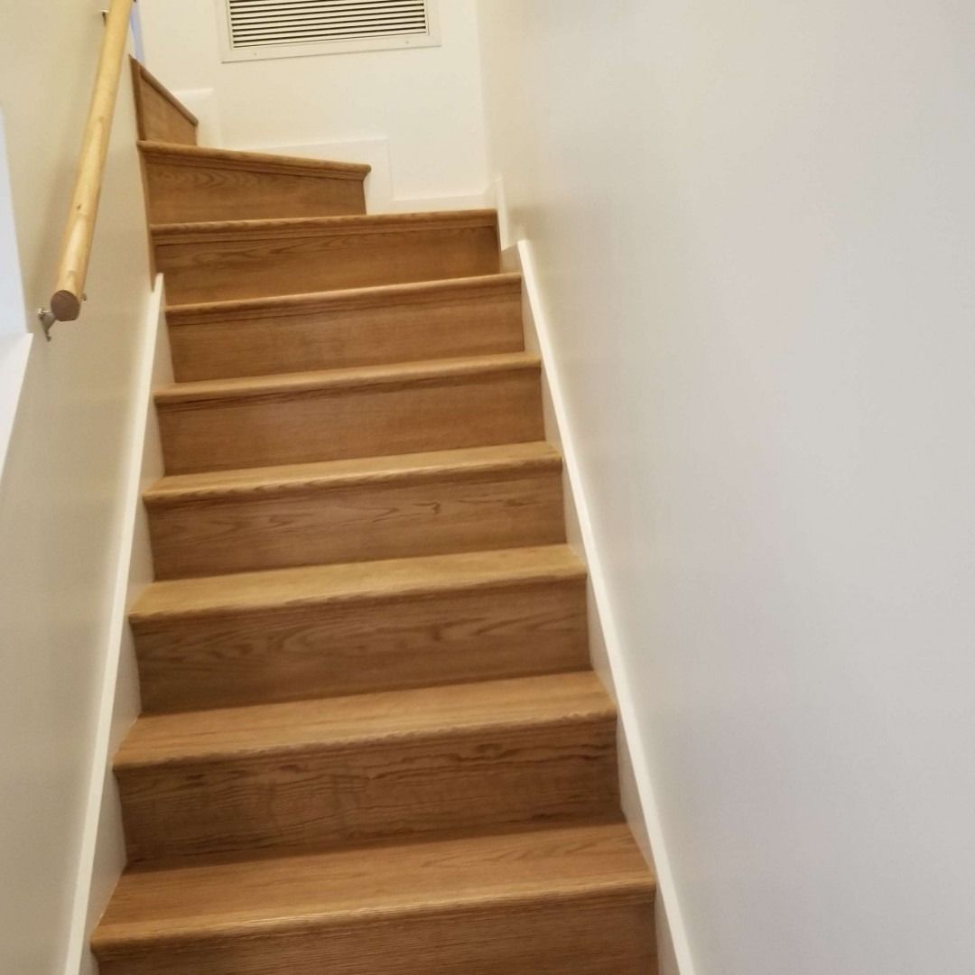 Wooden indoor staircase with a handrail, viewed from the bottom toward a landing.