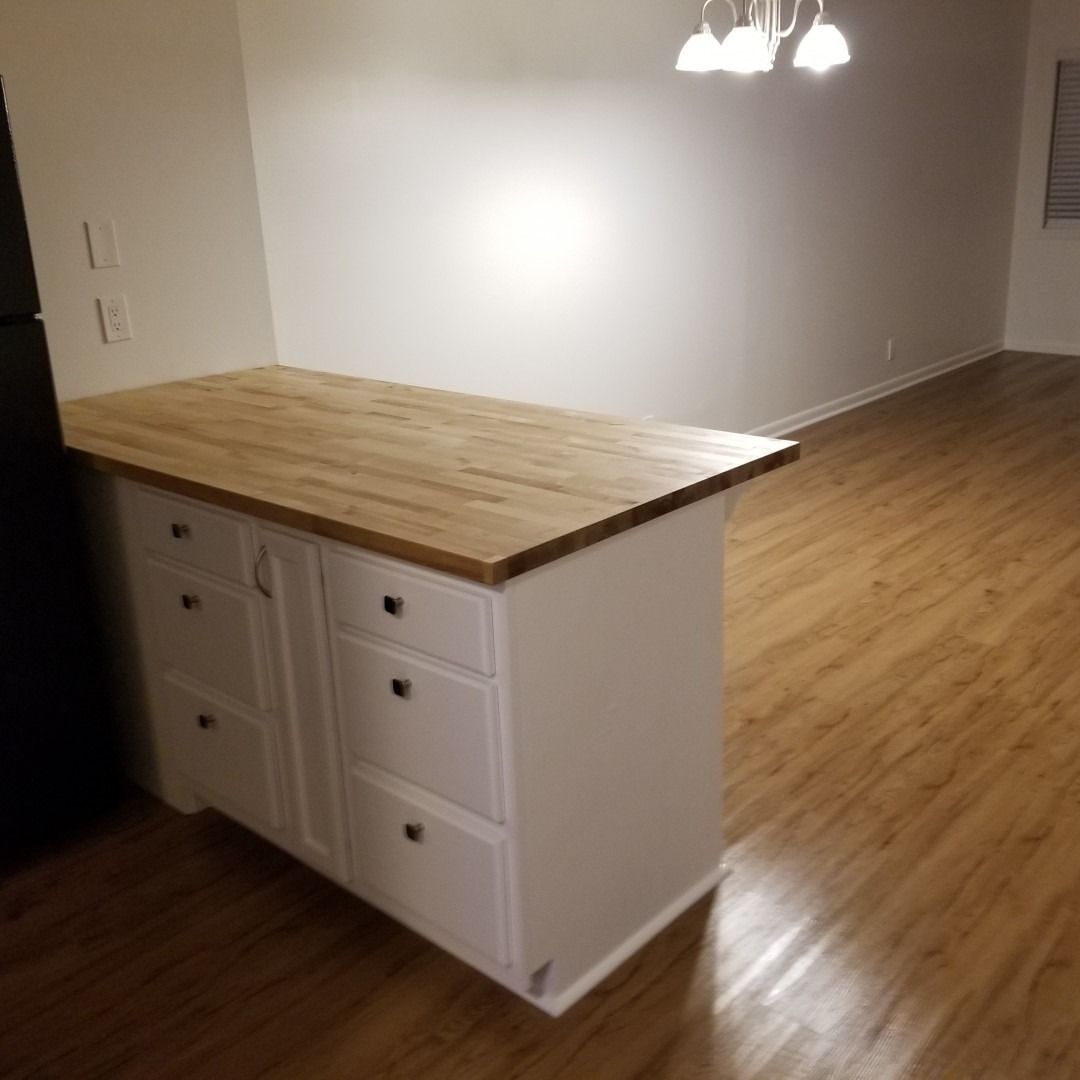 Small kitchen island with white cabinets and wooden countertop in an empty room with hardwood floors