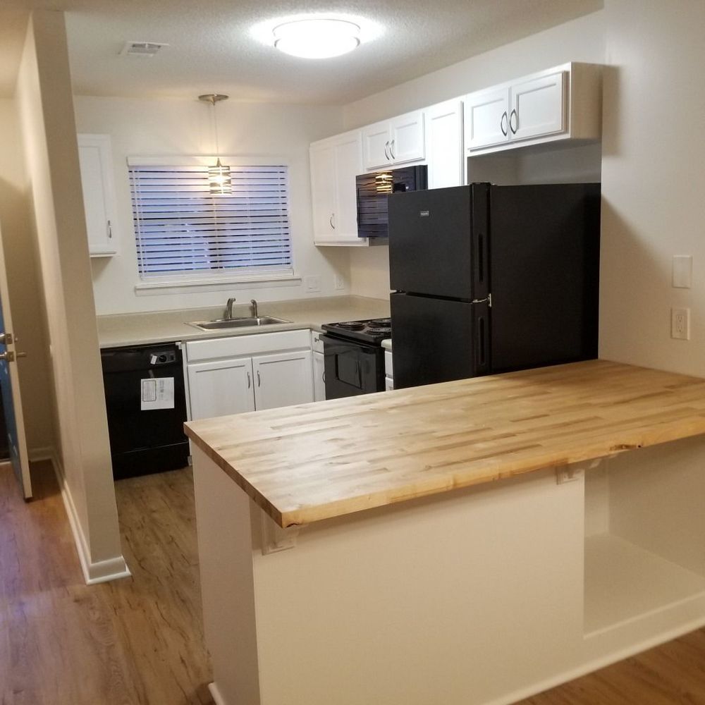 Small kitchen with black appliances, white cabinets, and a wooden breakfast bar.