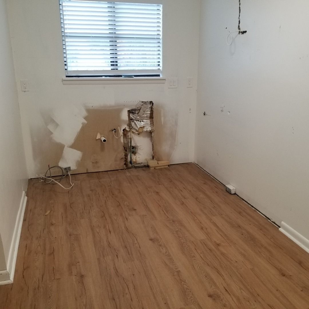 Empty room with wood flooring, a window, and damaged wall exposed behind a removed fixture.