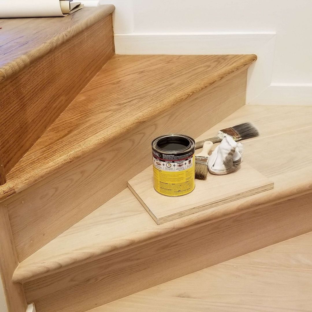 Stair landing with a can of yellow paint, brush, and a paint-splattered rag on a cardboard sheet