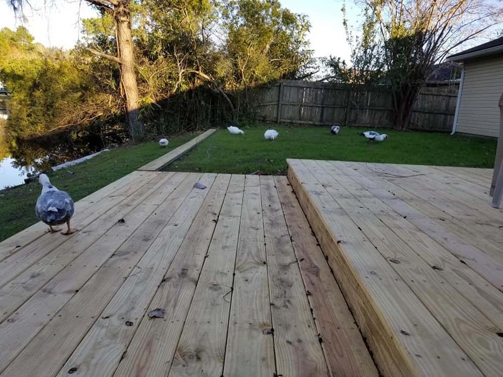 Backyard deck with two wooden platforms, grassy yard, fence, trees, and a blue-gray bird on the left deck.