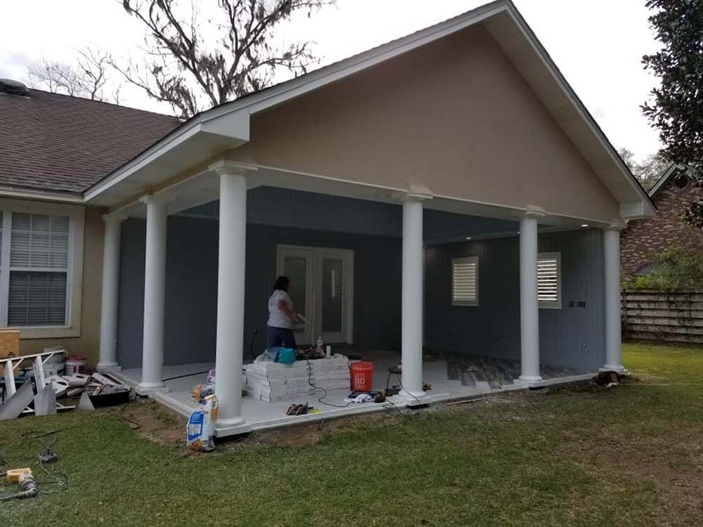Home porch under construction with white columns and a worker painting the covered patio