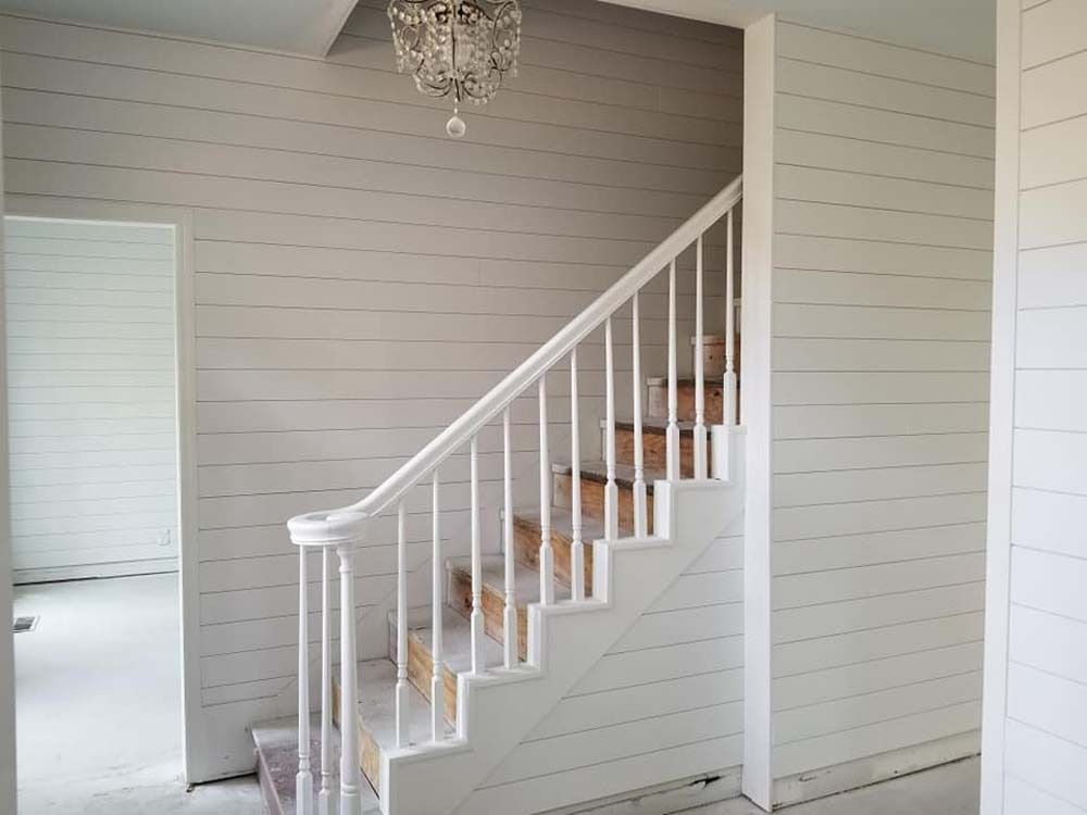 White staircase with wooden steps and railing in a light gray room with a chandelier