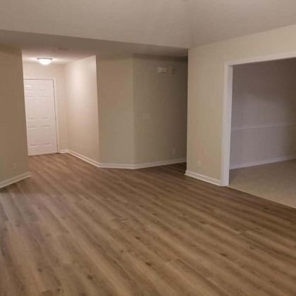 Empty beige room with wood flooring and an open doorway to a carpeted room