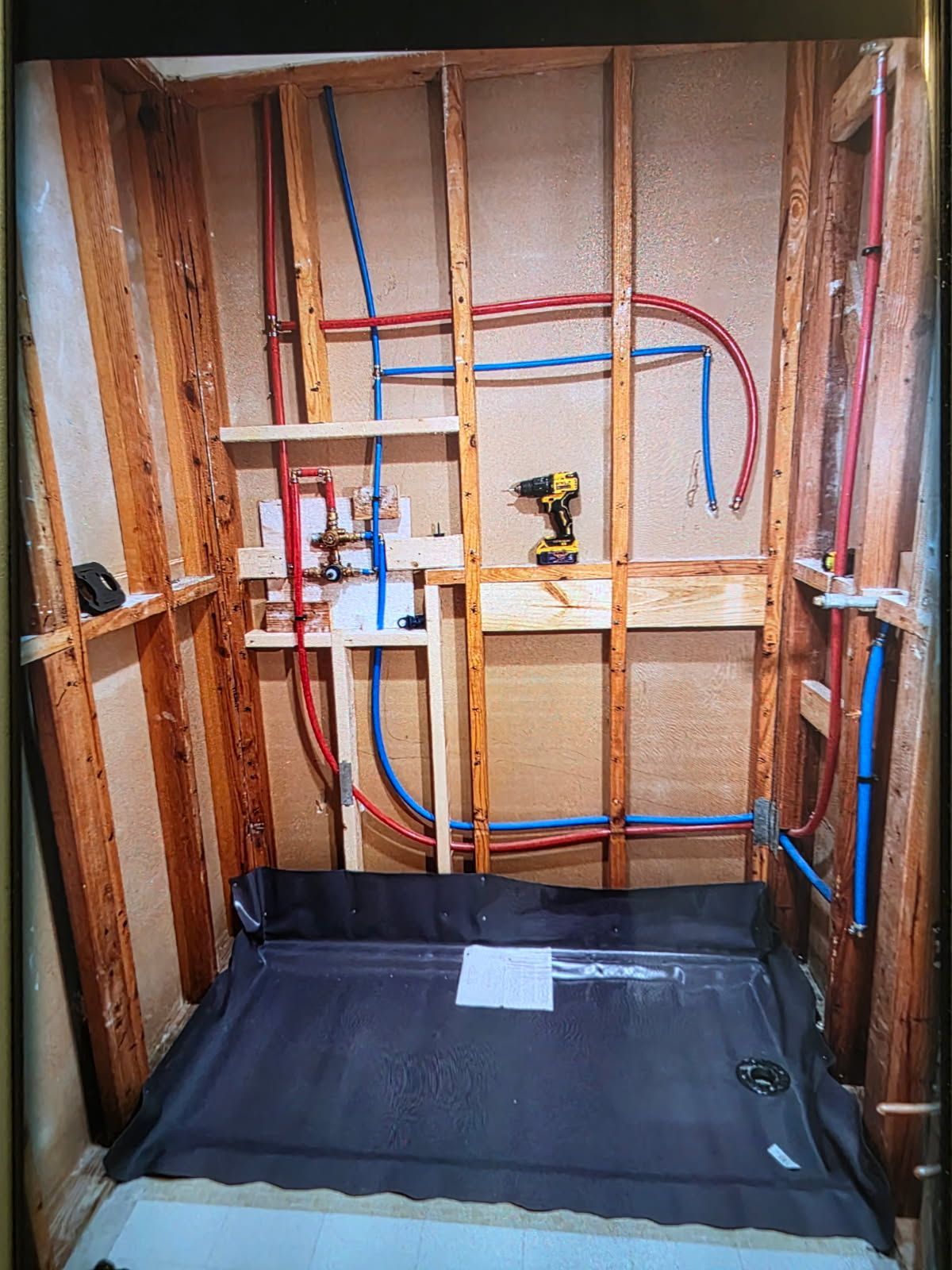 Framed bathroom wall with exposed plumbing and electrical lines above a waterproofed floor pan