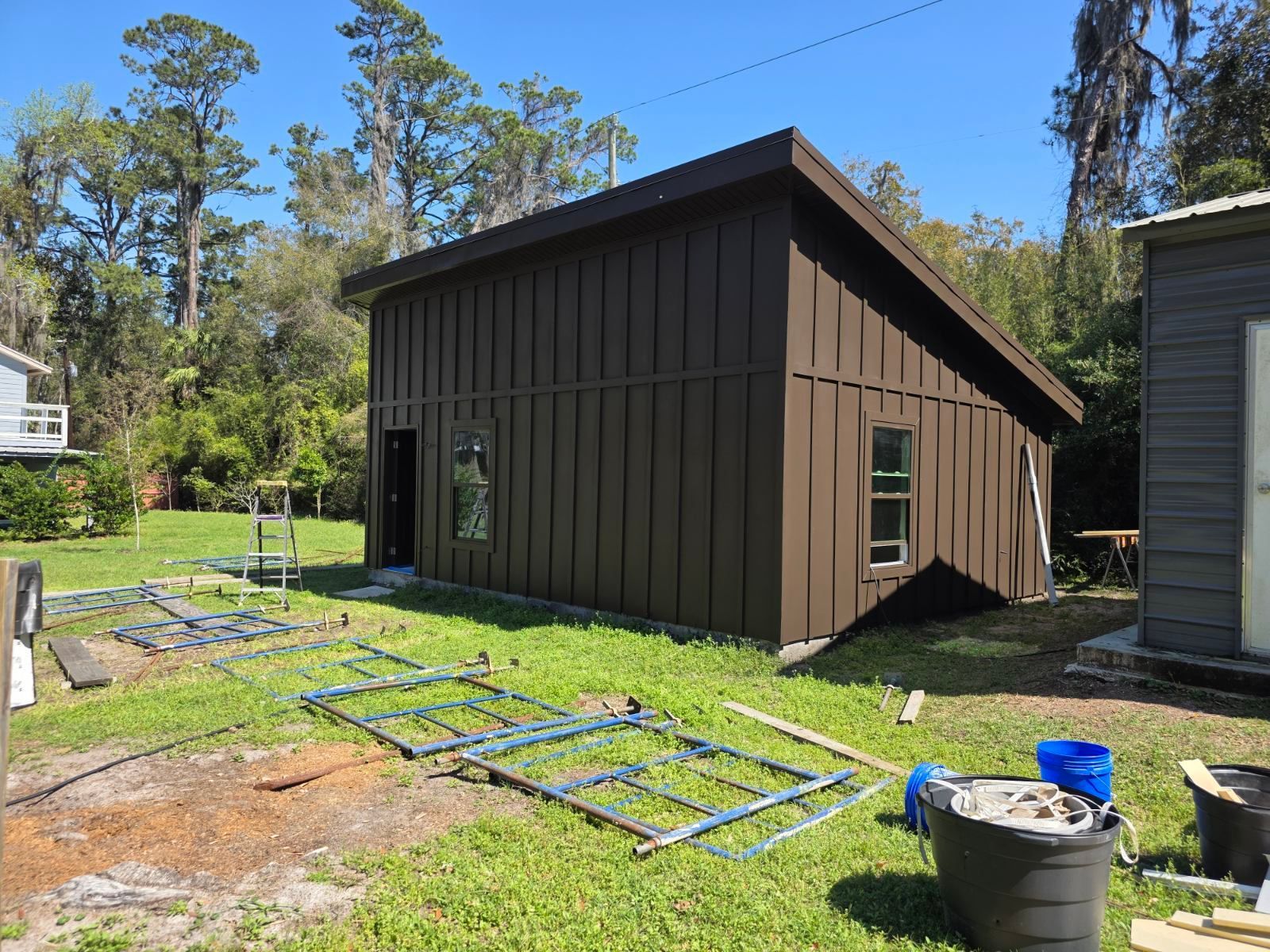 Brown shed under construction in a grassy yard, with ladder and building materials nearby.