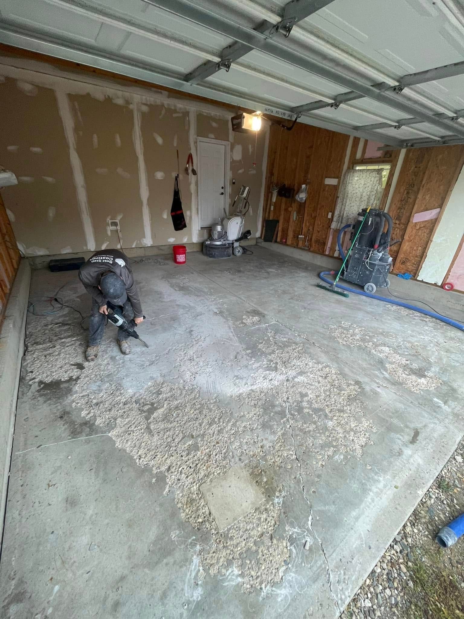 Person using a grinder in a garage. Concrete floor covered in debris; walls are unfinished.