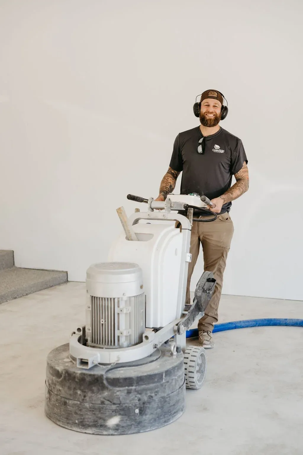 Man operating a floor grinder in a construction setting, wearing ear protection.