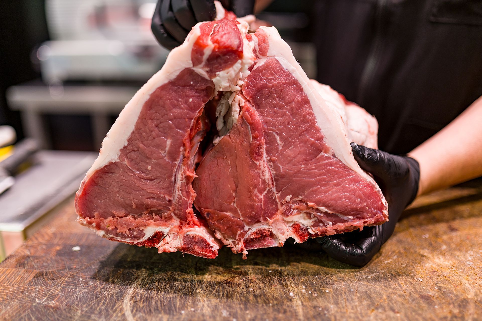 Un grosso taglio di manzo crudo tenuto aperto su un tagliere da mani guantate
