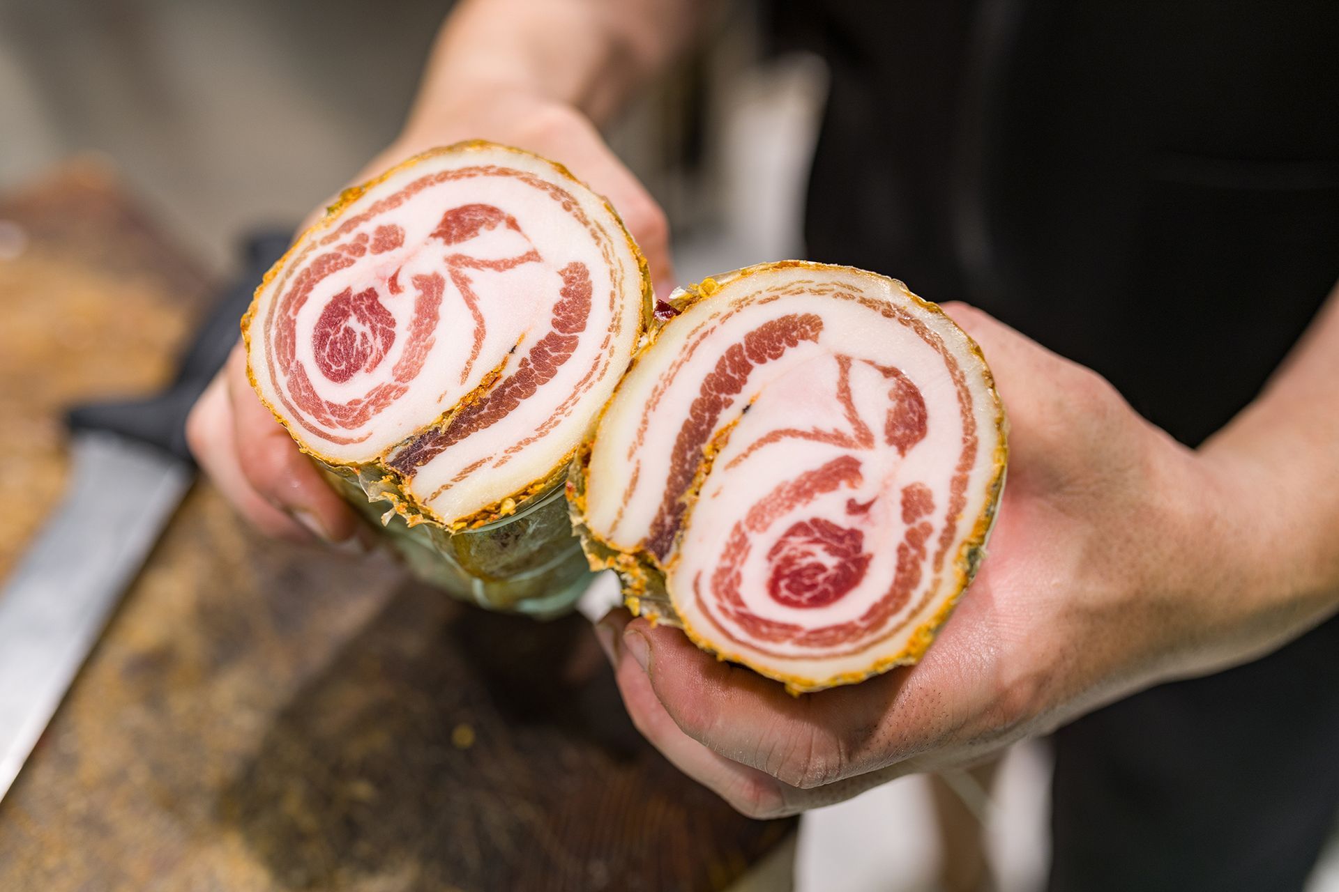 Mani che reggono due fette di carne arrotolata con spirali rosse su un tagliere