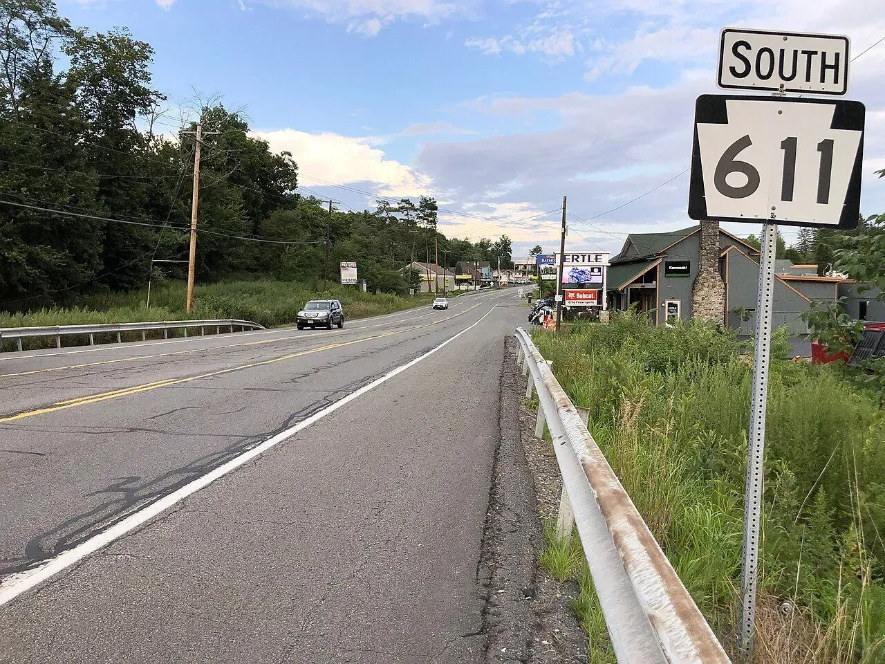 Roadside view of South Route 611 with a car, guardrail, and trees under a cloudy sky.