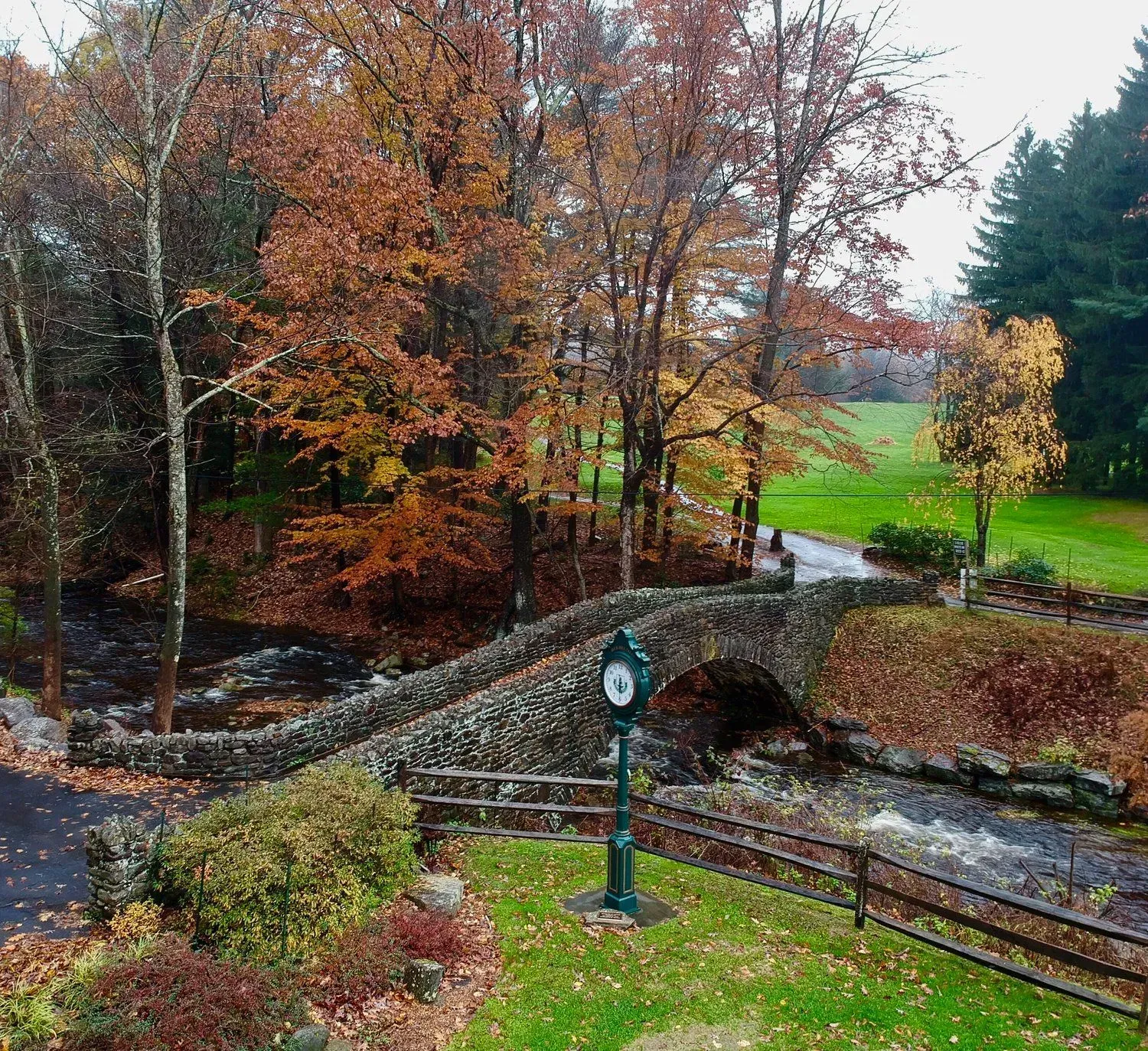 Autumn park with a stone bridge over a stream, surrounded by colorful trees and green grass