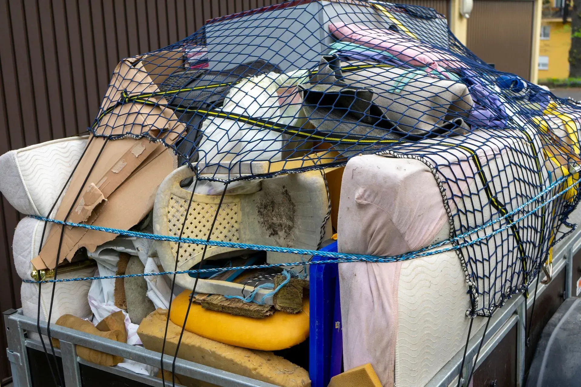 Overstuffed metal cart piled with bags, boxes, and a net cover outdoors
