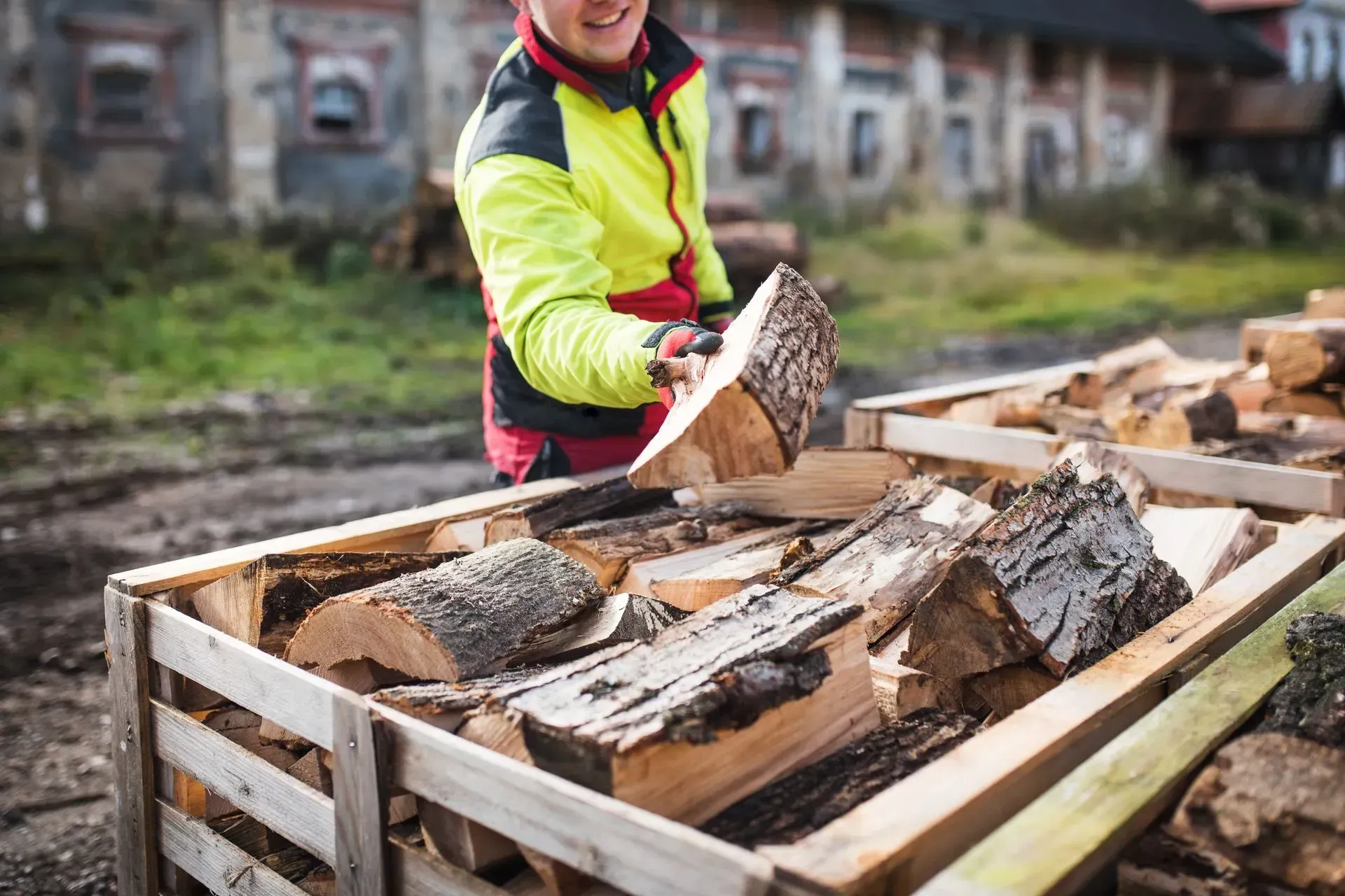 Person in a neon jacket loading firewood into a wooden crate outdoors.