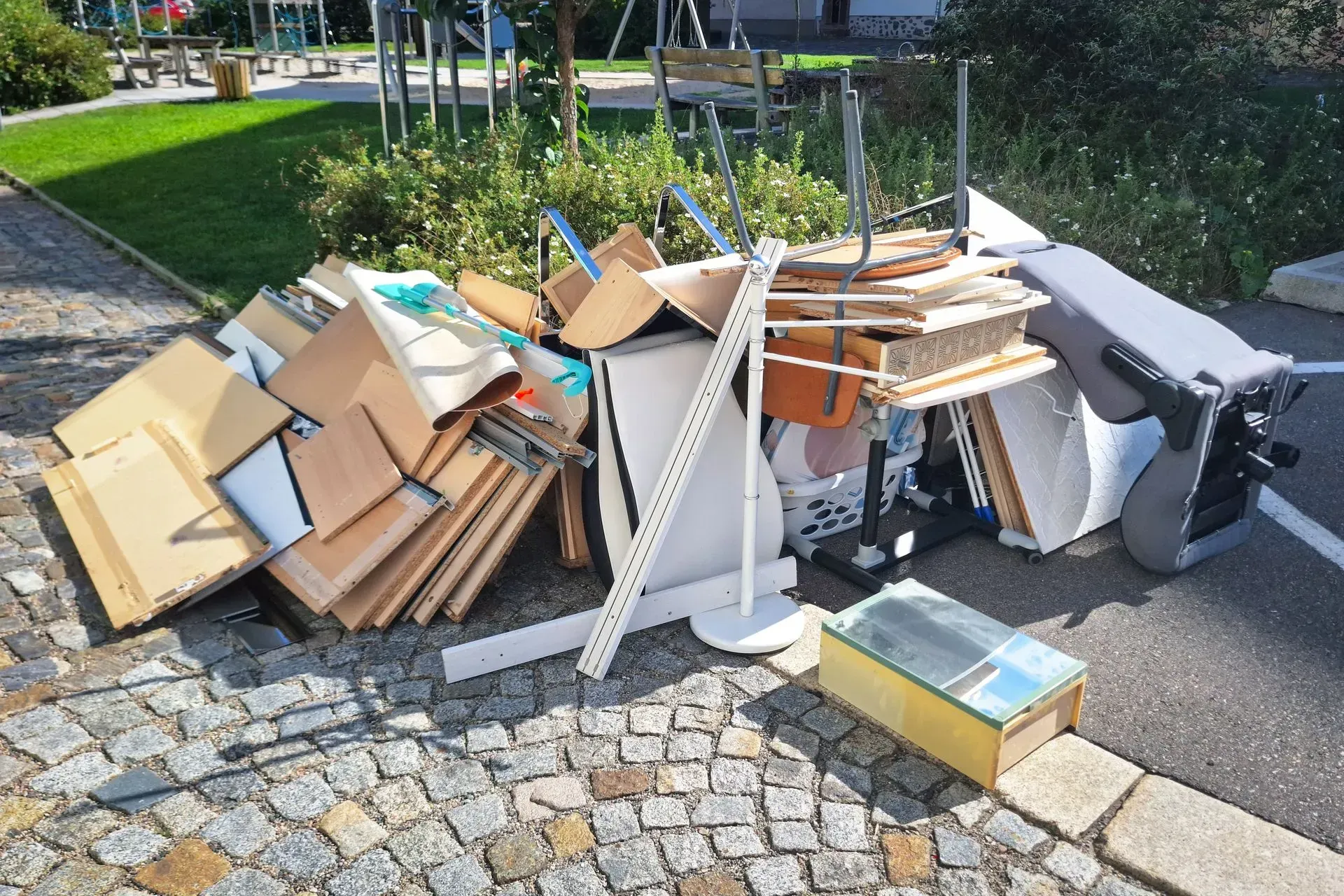 Overflowing pile of cardboard and mixed trash bags on a cobblestone sidewalk near a curbside bin