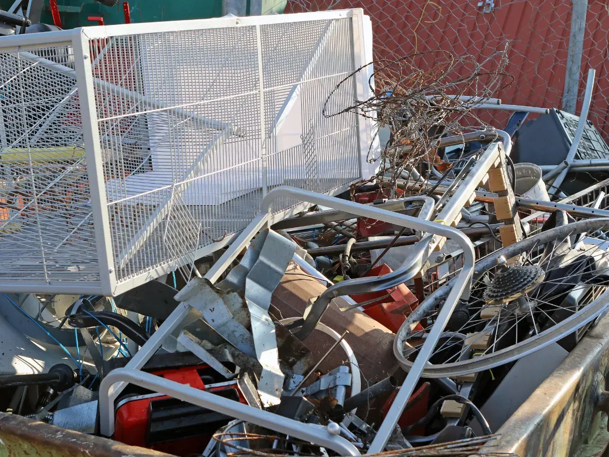 Pile of scrap metal and broken furniture in a junkyard, with a white metal cart on top.