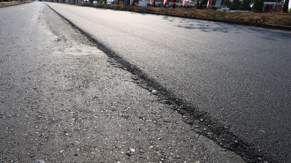A newly paved asphalt road section with a clear transition line between the rough old surface and the smooth new surface.