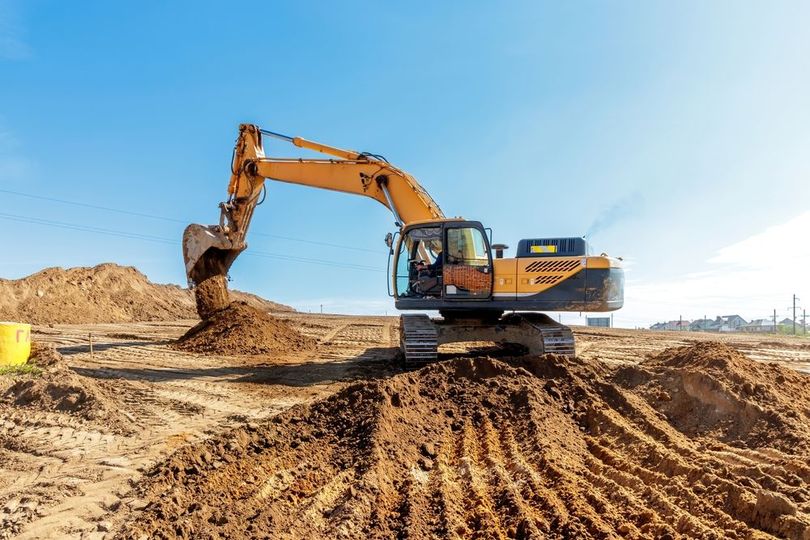 Yellow excavator digging in dirt at a construction site under a clear blue sky.