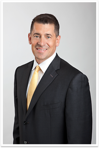 Man in a dark suit with a white shirt and yellow tie, posing against a light gray background