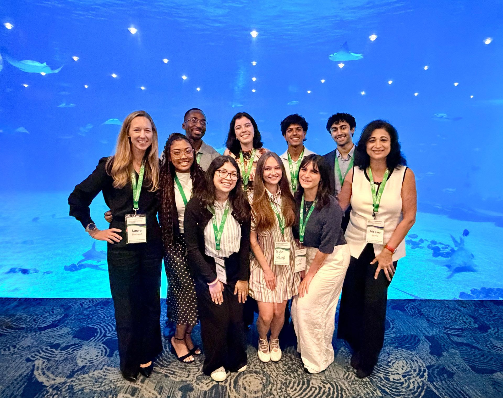 Group of nine people posing at an aquarium in front of a large blue underwater exhibit.