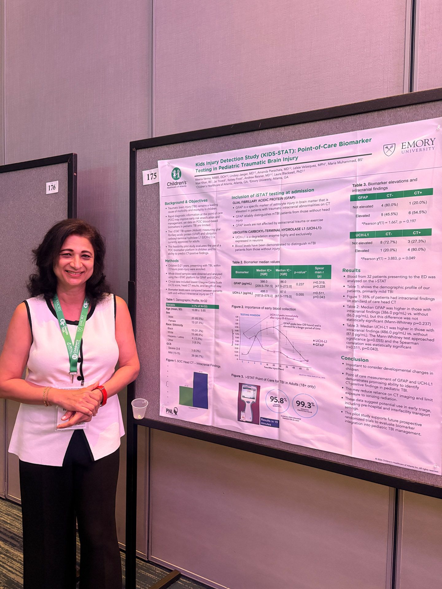 Woman standing beside a conference poster on a display board, smiling in a meeting room.